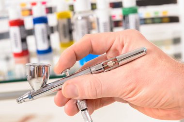 Hand holding a professional airbrush and bottles with paint clipart