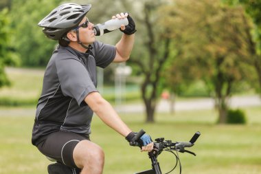 Bisikletçi bisiklet sürerken şişeden su içer