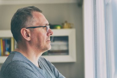 Bekar adam yalnızlık ve depresyondan muzdarip. Adam oturma odasında pencerenin yanında duruyor.