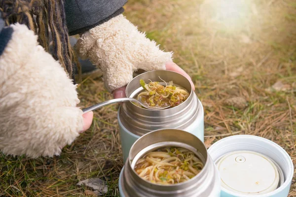 Warm food in a thermos standing on the grass. The concept of eating food outside and having a picnic