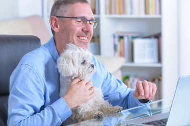 Adam evde çalışıyor ve küçük köpeğini tutuyor..