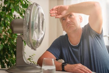 Adam evde sıcaktan muzdarip ve vantilatörün karşısında serinlemeye çalışıyor.