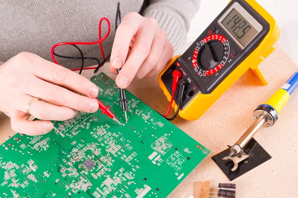 Serviceman checks PCB with a digital multimeter — Stock Photo, Image