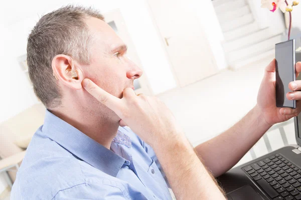 Slechthorende man aan het werk met laptop en mobiele telefoon — Stockfoto