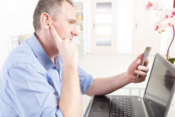 Uomo con problemi di udito che lavora con laptop e telefono cellulare — Foto Stock