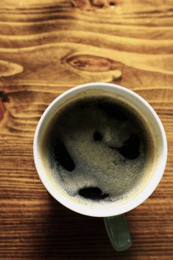 Tahta masadaki beyaz fincanda sıcak kahvenin üst görüntüsü.