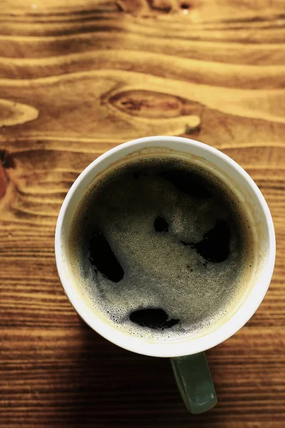 Tahta masadaki beyaz fincanda sıcak kahvenin üst görüntüsü.