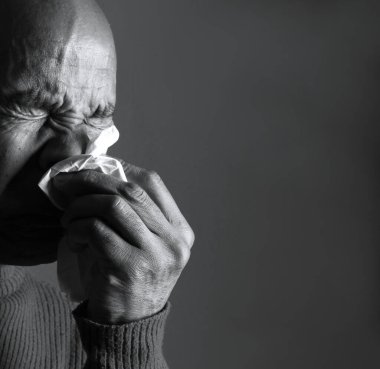 Adam karanlık arka planda üşüttükten sonra burnunu siliyor.