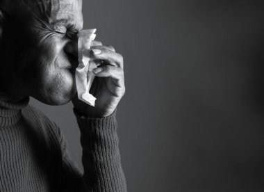 Adam karanlık arka planda üşüttükten sonra burnunu siliyor.