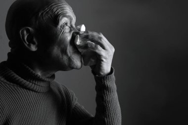 Adam karanlık arka planda üşüttükten sonra burnunu siliyor.