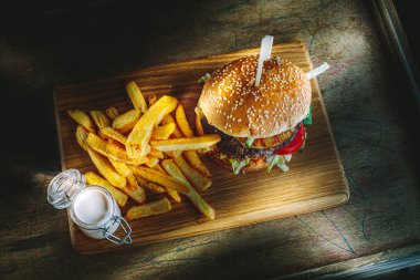 Lezzetli ev yapımı hamburger, patates kızartması ve ahşap masada sos, karamsar ışıklandırma..