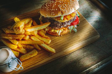 Lezzetli ev yapımı hamburger, patates kızartması ve ahşap masada sos, karamsar ışıklandırma..