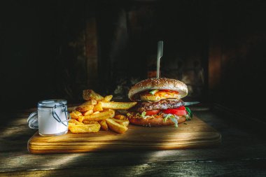 Lezzetli ev yapımı hamburger, patates kızartması ve ahşap masada sos, karamsar ışıklandırma..