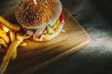 Lezzetli ev yapımı hamburger, patates kızartması ve ahşap masada sos, karamsar ışıklandırma..