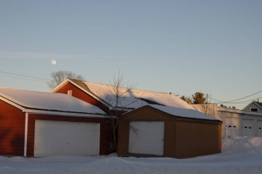 Kış boyunca karlı bir garaj ve mavi gökyüzünde bir ay.