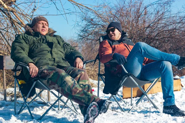 Dos jóvenes descansan en sillas de camping en el campamento en el día soleado, los amigos se relajan en la naturaleza, estilo de vida de invierno, Ulan-Ude, Rusia 24 Feb 2020 — Foto de Stock