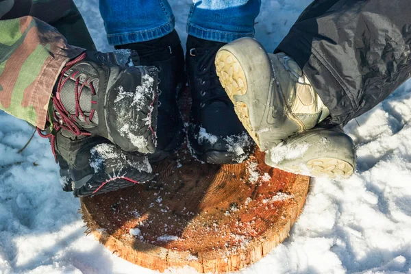 Piernas en botas de senderismo en reposapiés de madera, grupo de amigos descansan en el campamento en el soleado día de invierno, relajarse en la naturaleza — Foto de Stock