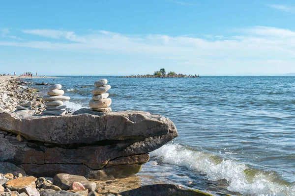 Piramidi di pietre impilate su roccia sulle onde costiere del lago Baikal, paesaggio marino, equilibrio e armonia concetto Immagine Stock