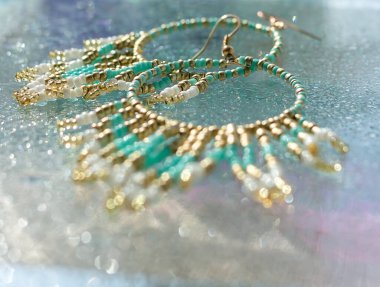 Altında parlak cam ve mavi arka plan bulunan turkuaz boho küpeler, plaj tatili tarzında yaz aksesuarları, tropik deniz mücevherleri konsepti, düşük açılı parlak görüntü.