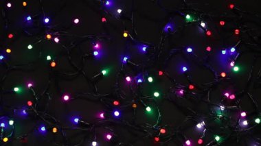 Yılbaşı dekoratif çelenklerinin bayram arkaplanı. Siyah arka planda. Çok renkli xmas ışıklarının yavaşça yanıp sönmesi.