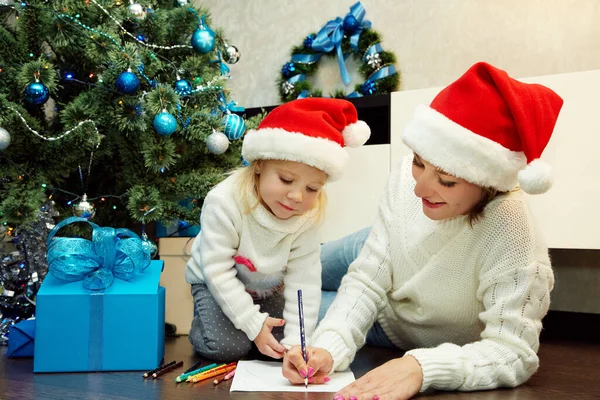 Madre felice e figlioletta scrivere una lettera a Babbo Natale Fotografia Stock