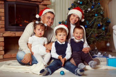 Aile evde kutlama yapıyor. Baba, anne ve çocuklar Noel ağacının arka planında.