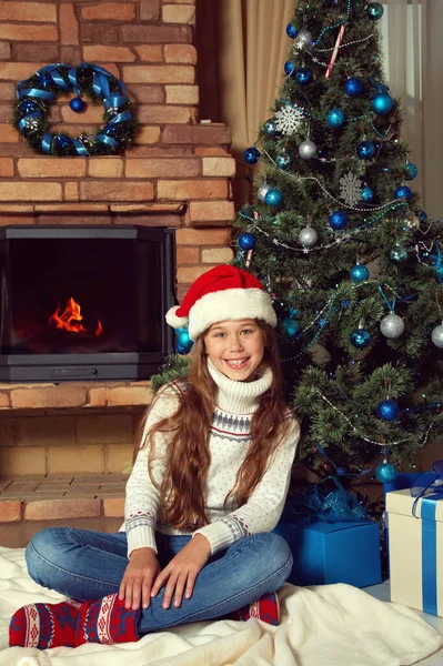 Nettes Teenager-Mädchen mit Weihnachtsmütze in der Nähe des Weihnachtsbaums. Weihnachtskind. — Stockfoto