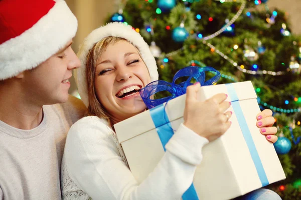 Jeune couple célébrant Noël à la maison. homme et femme en chapeau de Père Noël avec une boîte cadeau — Photo