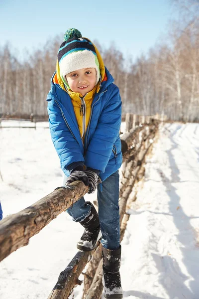 Komik küçük çocuk kışın çitin üzerinde oturuyor — Stok fotoğraf