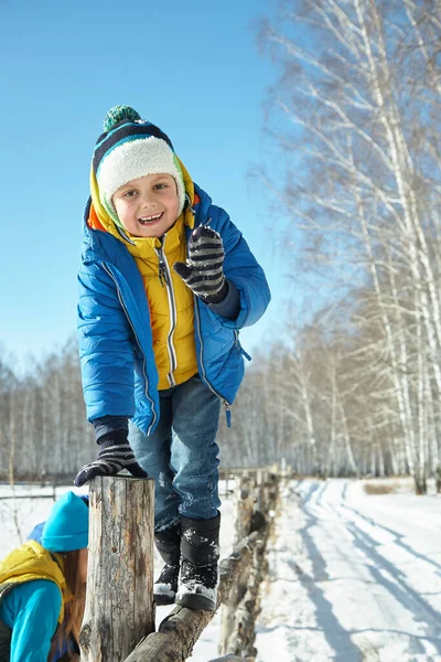 Grappig jongetje zittend op een hek in de winter — Stockfoto