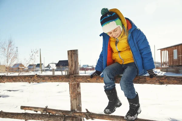 Grappig jongetje zittend op een hek in de winter — Stockfoto