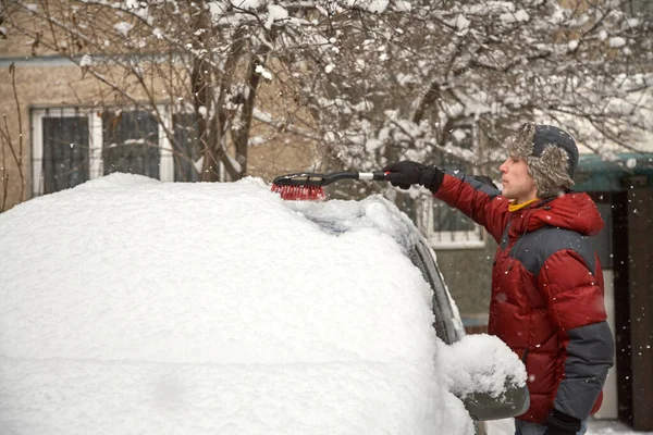 Un uomo spazzolando la neve dal parabrezza della sua auto Immagine Stock