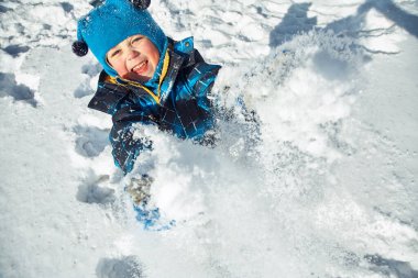 Komik küçük çocuk kışın karla oynuyor.