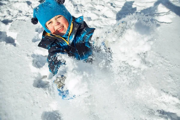 Komik küçük çocuk kışın karla oynuyor.