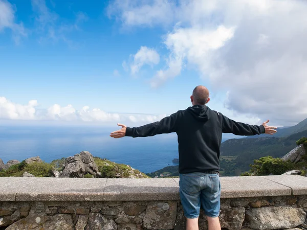 Homem com braços estendidos em frente a uma paisagem costeira — Fotografia de Stock