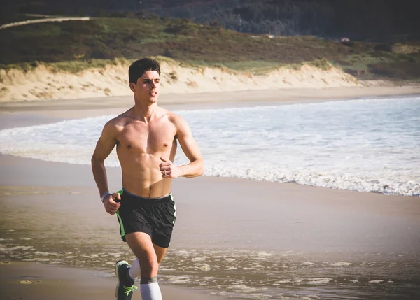 Joven hombre sin camisa corriendo a lo largo de la playa —  Fotos de Stock