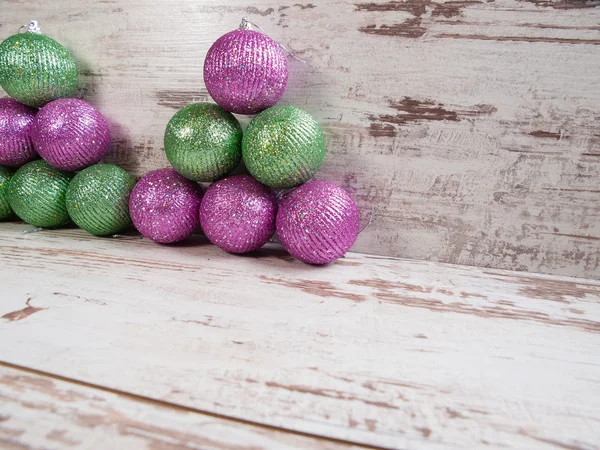 Roze en groene kerstballen in een stapel op houten achtergrond — Stockfoto