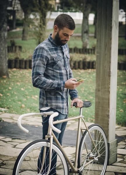 Hipster hombre con una bicicleta fixie y teléfono inteligente — Foto de Stock