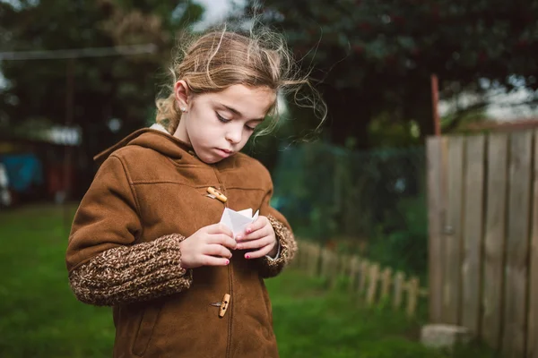 Little girl playing with a piece of paper outdoors — Stock Photo, Image