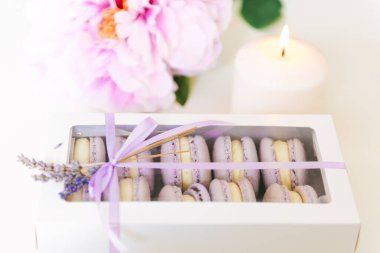 Beyaz masadaki renkli kurabiyeler. Mum ve lavantanın yanındaki hediye kutusundaki kurabiyeye bak. Seçici odak noktası.