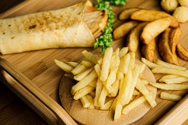 Muhtelif patatesler. Domates sosuyla servis edilen ahşap bir tabakta kızartılmış patates. Cips dilimleri, patates püresi, ekmek arası patates topları ve kızarmış köy tarafı..