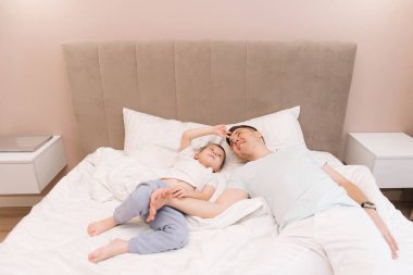 Genç baba, bebeğiyle oynuyor ve gülüyor. Oğlu evde, yatakta, mutlu bir aile.