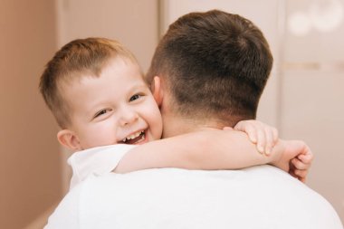 Genç baba, bebeğiyle oynuyor ve gülüyor. Oğlu evde, yatakta, mutlu bir aile.
