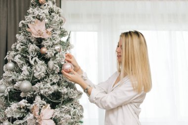 Güzel, genç, sarışın, gülümseyen kız yeni yıl için evi dekore ediyor.