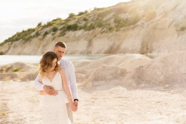 Birbirlerine aşık güzel bir çift, bir erkek ve bir kadın, gün batımında mavi bir göl ve kum kenarında öpüşürler. Sahilde deniz tatili, gün batımı, sabah, balayı, tropik hava, okyanus, kız, ilişki..