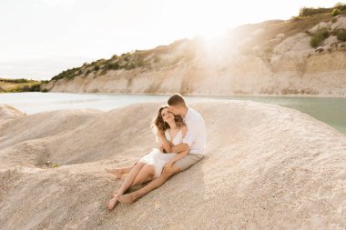 Birbirlerine aşık güzel bir çift, bir erkek ve bir kadın, gün batımında mavi bir göl ve kum kenarında öpüşürler. Sahilde deniz tatili, gün batımı, sabah, balayı, tropik hava, okyanus, kız, ilişki..