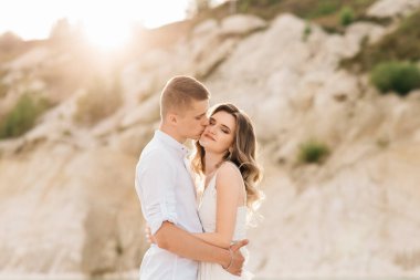 Birbirlerine aşık güzel bir çift, bir erkek ve bir kadın, gün batımında mavi bir göl ve kum kenarında öpüşürler. Sahilde deniz tatili, gün batımı, sabah, balayı, tropik hava, okyanus, kız, ilişki..