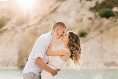 Birbirlerine aşık güzel bir çift, bir erkek ve bir kadın, gün batımında mavi bir göl ve kum kenarında öpüşürler. Sahilde deniz tatili, gün batımı, sabah, balayı, tropik hava, okyanus, kız, ilişki..