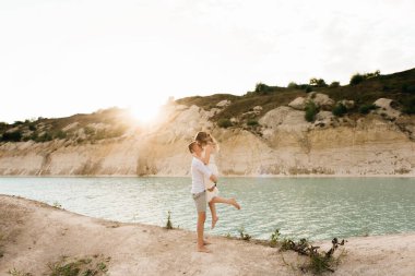 Birbirlerine aşık güzel bir çift, bir erkek ve bir kadın, gün batımında mavi bir göl ve kum kenarında öpüşürler. Sahilde deniz tatili, gün batımı, sabah, balayı, tropik hava, okyanus, kız, ilişki..