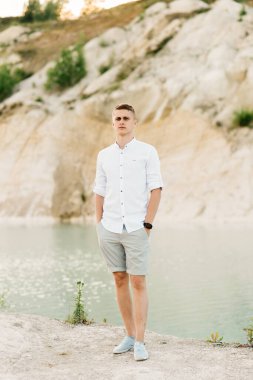 Güzel genç adam mavi bir göl ve gün batımında kumla dünyayı dolaşır.